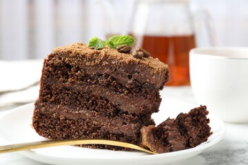 Piece of delicious chocolate cake with coffee beans, mint and fork on white marble table, closeup