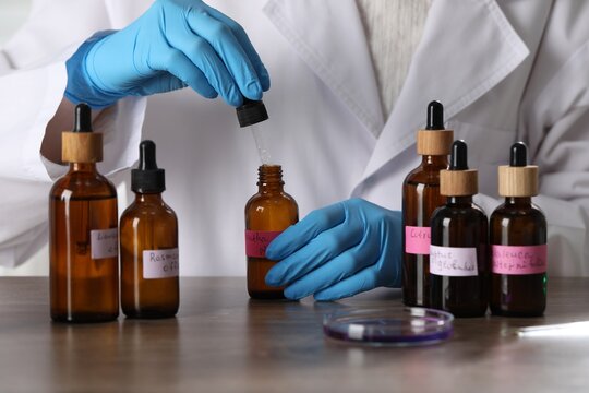 Professional perfumer developing luxury perfume at wooden table in laboratory, closeup