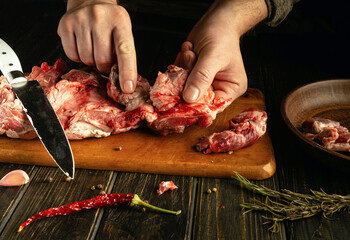 Hands skillfully separate fresh meat on a wooden cutting board, surrounded by herbs and spices. The warm light enhances the vibrant colors, creating a homey atmosphere