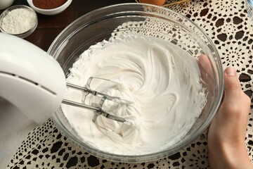 Woman whisking cream with hand mixer at table, closeup