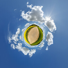 simple little tiny planet without buildings in blue sky with sun and beautiful clouds. Transformation of spherical panorama 360 degrees. Spherical abstract aerial view. Curvature of space.