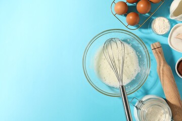 Whisk, egg whites in bowl and other products on light blue table, flat lay. Space for text