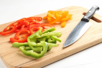 Slices of fresh colorful bell peppers and knife on white wooden table, closeup