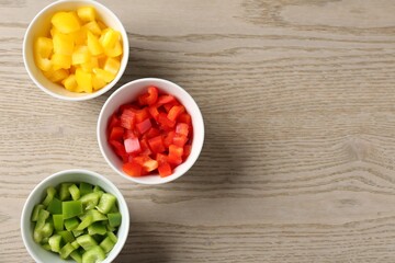 Pieces of fresh colorful bell peppers in bowls on wooden table, flat lay. Space for text
