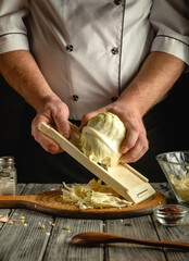 A chef skillfully slices a fresh cabbage with a mandoline on a wooden board in a warmly lit...