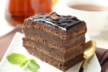 Piece of chocolate cake served with mint, spoon and tea on table, closeup