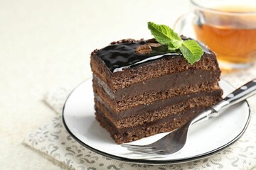 Piece of chocolate cake served with mint, fork and tea on white table, closeup