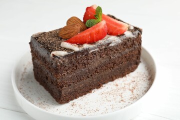 Piece of delicious chocolate cake with strawberry and almonds on white table, closeup