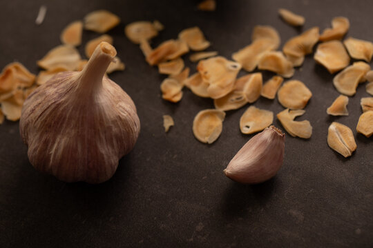 Garlic bulb with clove and garlic chips on dark benchtop