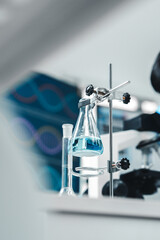 An Erlenmeyer flask filled with blue liquid is clamped in place in a science lab, symbolizing...