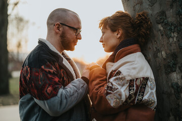 A loving couple standing by a tree, gazing into each other's eyes during sunset.
