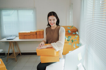 Young asian woman entrepreneur, owner of a small business, is checking online orders from customers before shipping them, she is smiling and looking at her computer