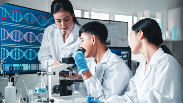 Group of young scientists in lab coats collaborate in a high-tech laboratory, analyzing samples through a microscope and documenting results, symbolizing innovation, teamwork, and modern research. - Powered by Adobe