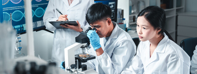 Group of young scientists in lab coats collaborate in a high-tech laboratory, analyzing samples...