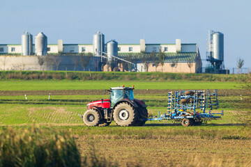 Red tractor plowing agricultural field near biogas plant