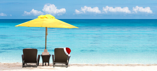 Santa Claus hat on sunbed on tropical beach with sun umbrellas and chaise-longues. Christmas celebration