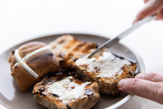 buttering toasted hot cross buns for Easter