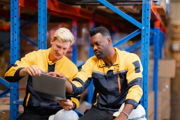 Warehouse supervisors wearing safety gear collaborate on operations while analyzing reports on a...