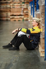 A young man sits down in a warehouse, leaning back with tired eyes. He’s clearly exhausted and...