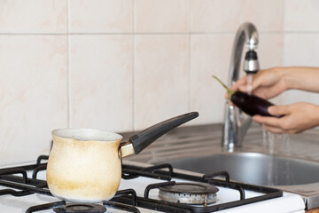 Turk on the stove and a woman washing an eggplant under the tap in the kitchen, cooking, household environment