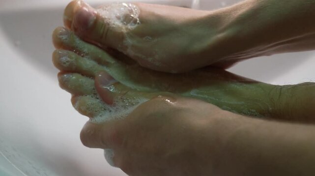 Wet male feet in the sink close-up.
Naked man washes his heels in the bathroom.
Man takes spa treatments.
Cleanliness and hygiene of feet.
Freshness of feet.
Skin health.
Sweaty feet
