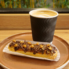 Hot Milk Coffee and Sweet Chocolate Eclair Decorated with Gilded Nuts and Chocolate Icing 
