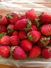 Top-down close-up of a plastic container filled with fresh red strawberries, some with natural flaws ideal for themes of fresh produce, healthy eating, shoppin