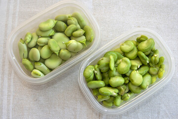 Fresh and peeled broad beans in plastic containers