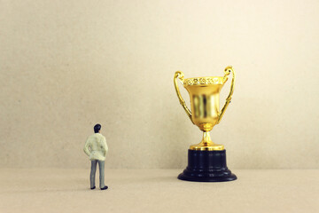 Concept image of miniature figure looking at trophy. Idea of leadership and inspiration