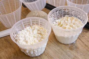 Cheesemaker preparing fresh ricotta cheese using plastic draining baskets and sieve