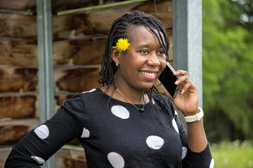 Smiling African Woman Talking on Smart phone Outdoors with Yellow Flower in Hair