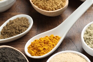 Different superfood powders in bowls and spoons on wooden table, closeup