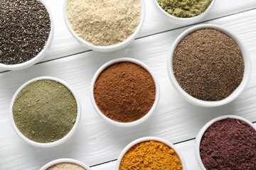 Different superfood powders in bowls on white wooden table, flat lay