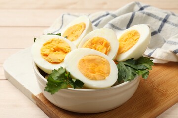 Boiled eggs and parsley in bowl on wooden table, closeup