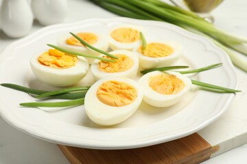 Halves of hard boiled eggs with green onions on white table, closeup