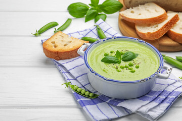 Tasty pea cream soup with basil served on white wooden table