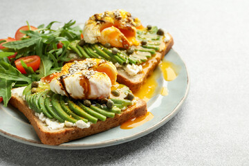 Delicious sandwiches with avocado, poached egg, salmon, tomatoes and arugula on gray table, closeup