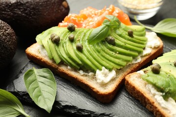 Delicious sandwiches with avocado, salmon, cream cheese, basil and capers on table, closeup