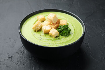 Tasty pea cream soup with croutons and broccoli on black table, closeup