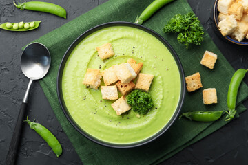 Tasty pea cream soup with croutons and broccoli served on black table, flat lay