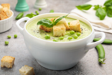 Tasty pea cream soup with croutons and basil served on grey table, closeup