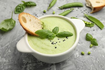 Tasty pea cream soup with basil and crouton served on grey table, closeup