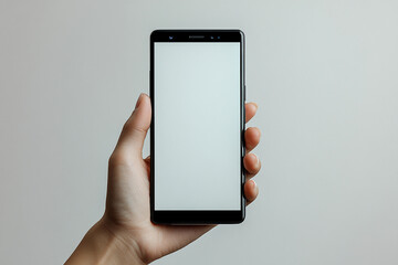 Hand holding a modern black smartphone with a blank white screen against a gray background