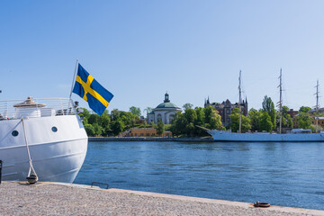 Stockholm, Sweden, swedish flag infront of the island of Skeppsholmen, with historical buildings and sail boats.