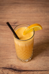 A refreshing glass of freshly squeezed orange juice sits on a wooden table, radiating natural color...