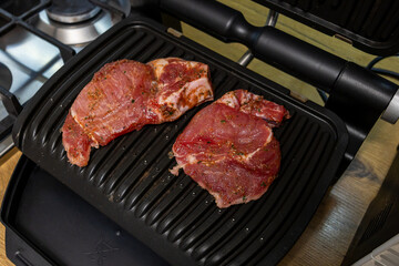 Grilled marinated meat cooking on an electric contact grill in a modern kitchen.