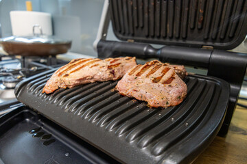 Grilled marinated meat cooking on an electric contact grill in a modern kitchen.