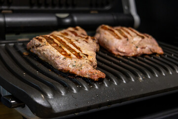 Grilled marinated meat cooking on an electric contact grill in a modern kitchen.