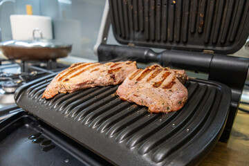 Grilled marinated meat cooking on an electric contact grill in a modern kitchen.