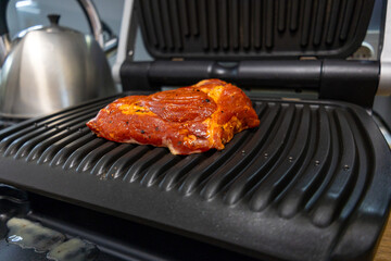 Grilled marinated meat cooking on an electric contact grill in a modern kitchen.